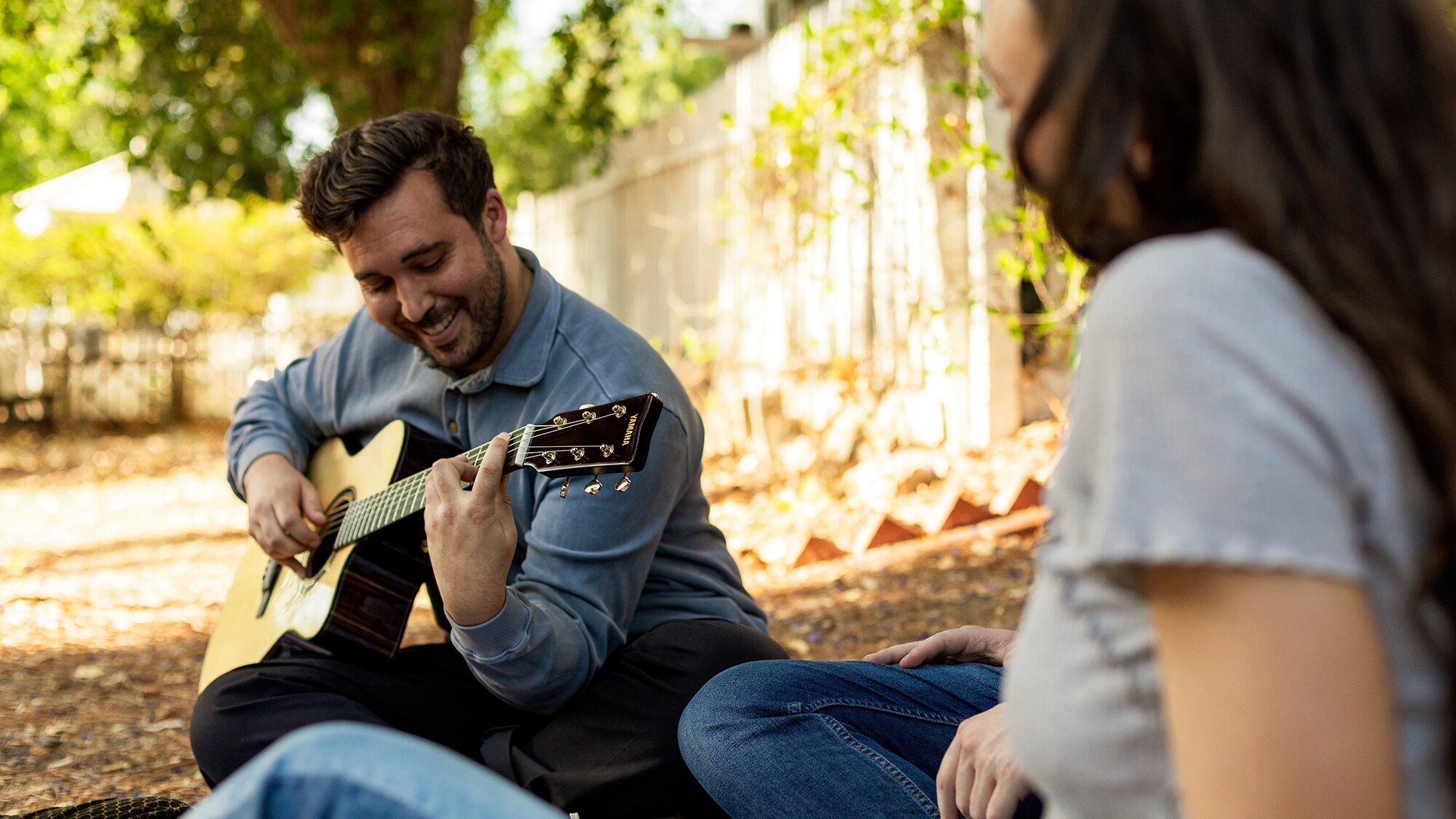 Man smiling while playing the TAS3 C acoustic guitar outdoors.